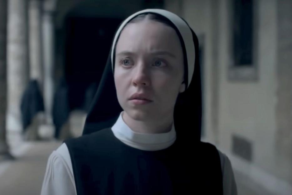 Eine junge Nonne mit ernstem Blick steht in einem Klostergang.
