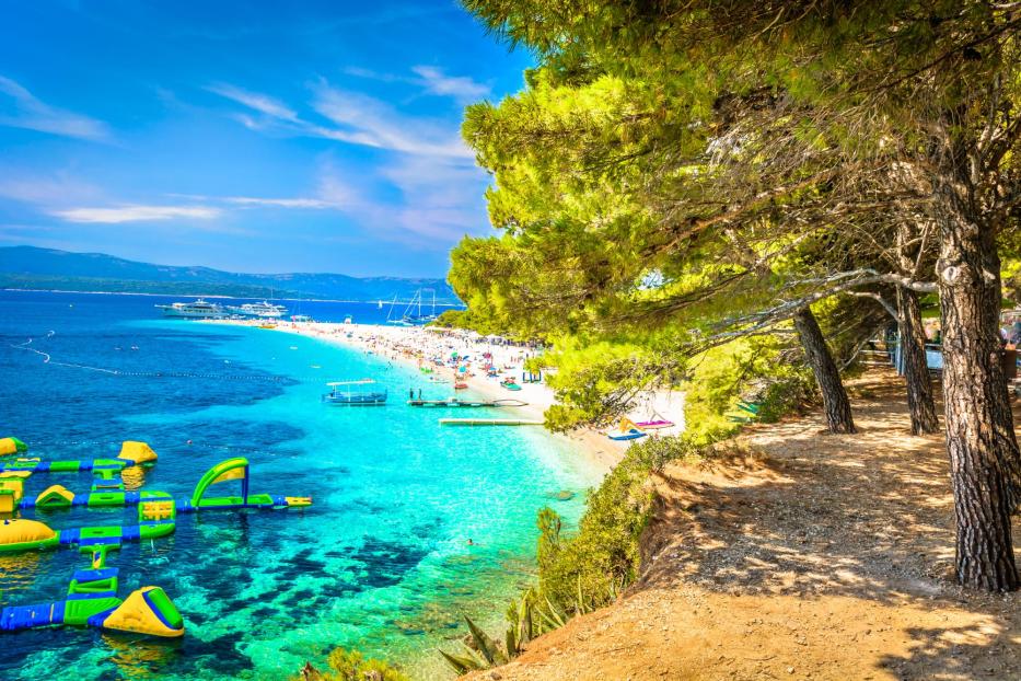Ein belebter Strand mit türkisfarbenem Wasser und einer aufblasbaren Wasserspielanlage.
