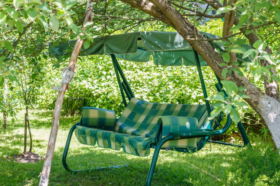 Eine grüne Gartenschaukel steht im Schatten eines Baumes.