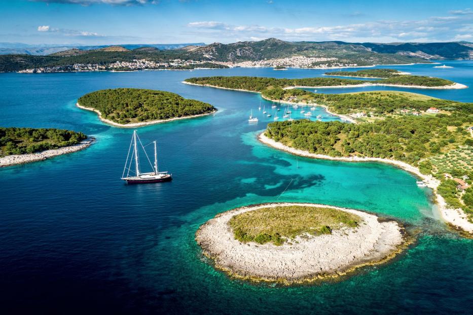 Eine Segelyacht ankert in einer Bucht mit türkisfarbenem Wasser und kleinen Inseln.