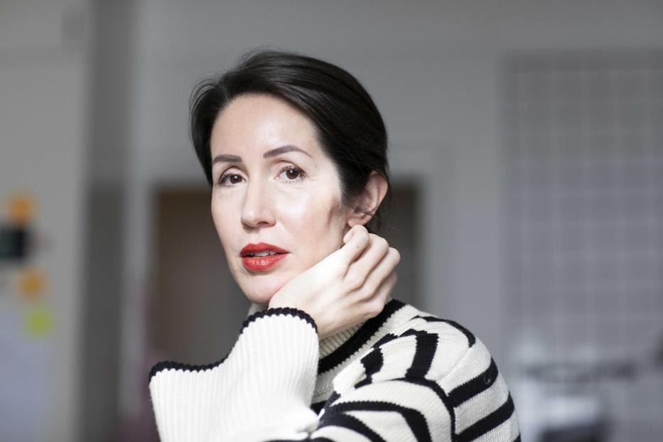 Eine Frau mit dunklen Haaren und rotem Lippenstift trägt einen schwarz-weiß gestreiften Pullover.