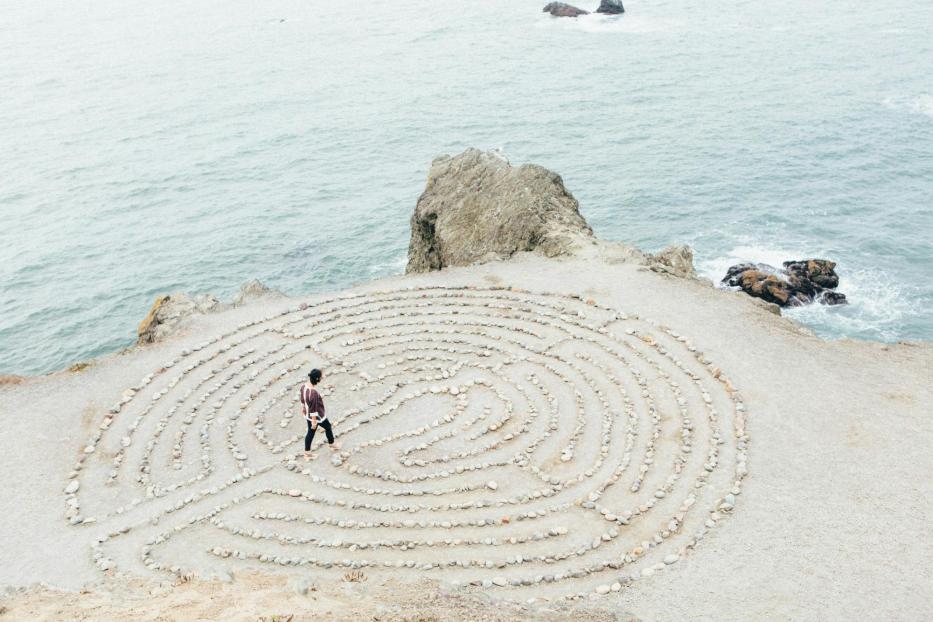 Eine Person geht durch ein Steinlabyrinth auf einer Klippe am Meer.