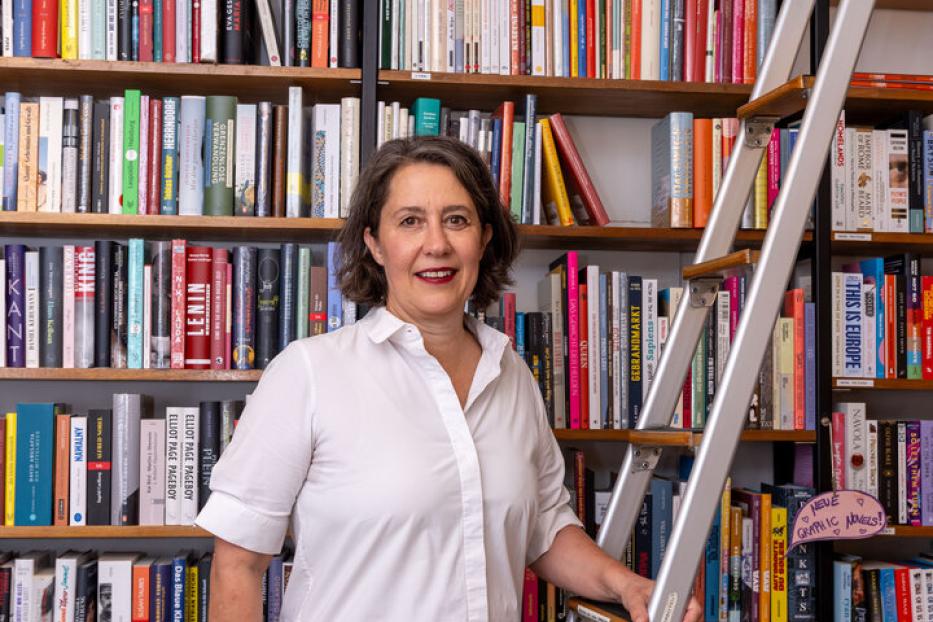 Eine Frau steht vor einem Bücherregal mit einer Leiter.