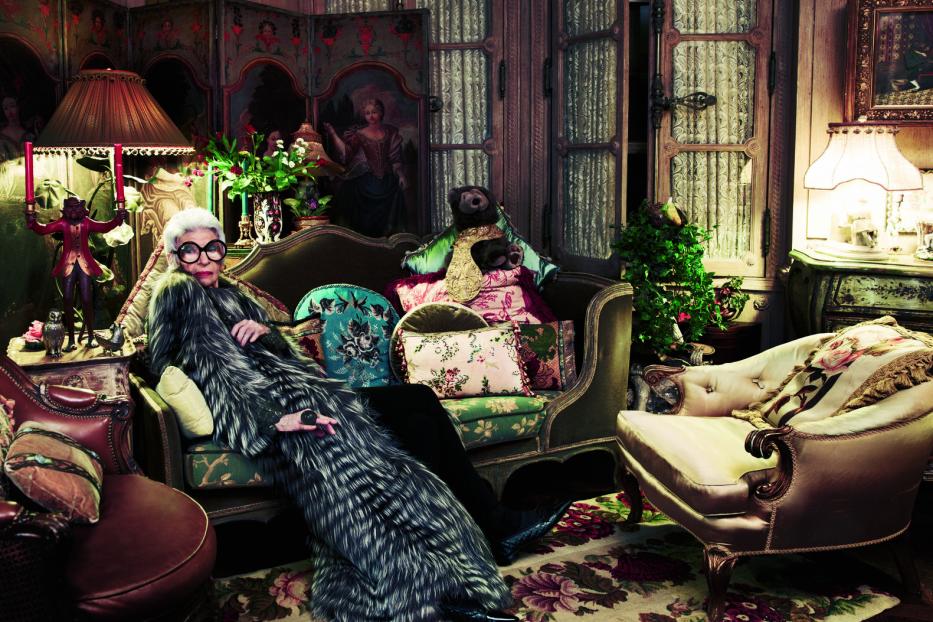 Iris Apfel ruht in einem opulenten Interieur auf einem Sofa.
