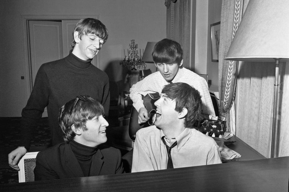 Die Beatles posieren mit Gitarre und Klavier in einem Raum.