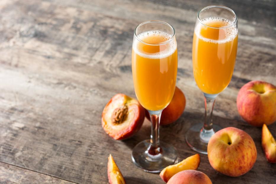 Zwei Gläser Bellini und Pfirsiche auf einem Holztisch.