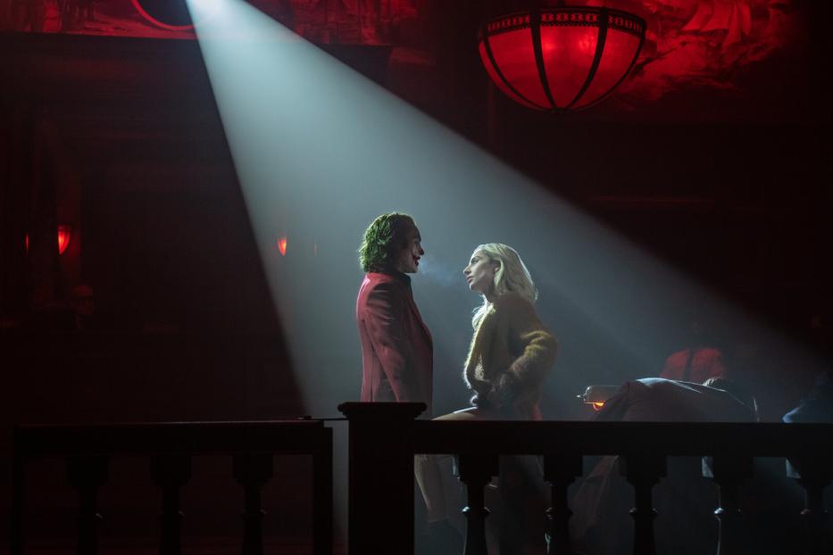 Der Joker im roten Anzug steht im Scheinwerferlicht mit Harley Quinn mitten in einem dunklen Gerichtssaal.