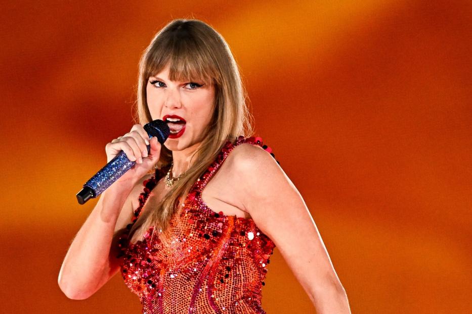 Taylor Swift singt in einem roten Paillettenkleid in ein glitzerndes Mikrofon.