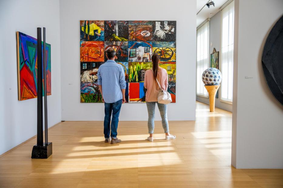 Zwei Personen betrachten ein großes, farbenfrohes Gemälde in einer Kunstgalerie.