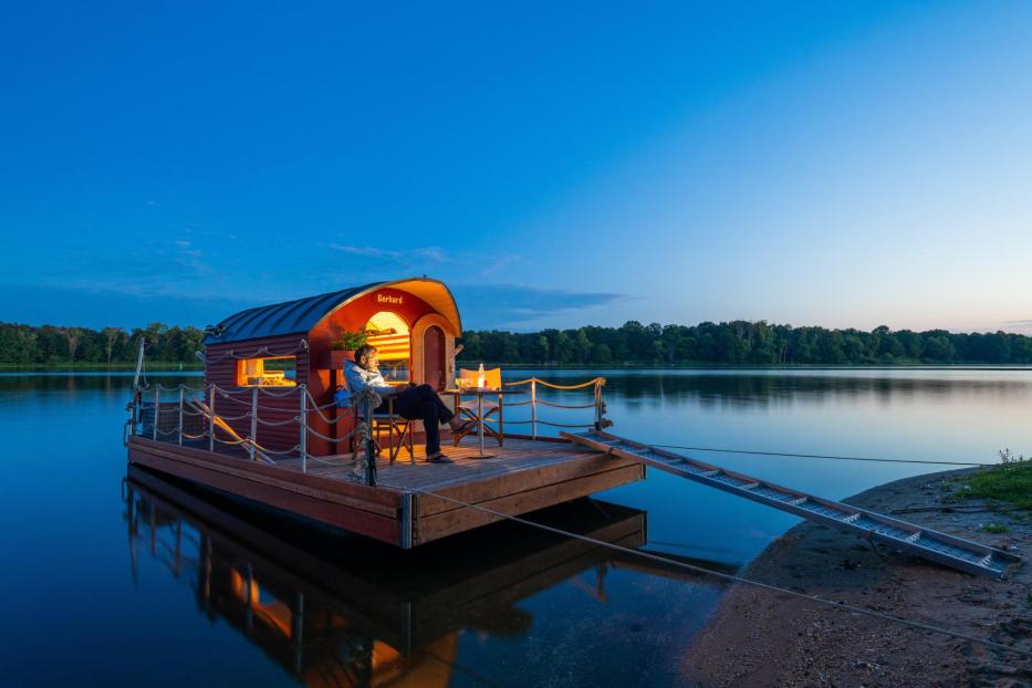 Ein Mann sitzt am Abend auf einem schwimmenden Haus auf einem See.