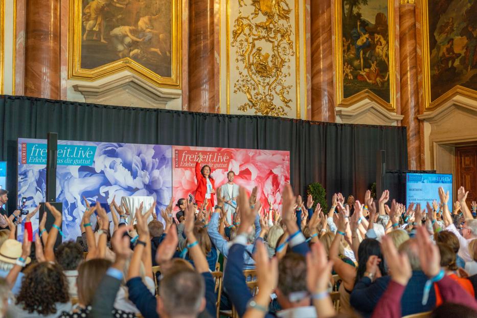 Ein barocker Festsaal mit vielen Besuchern, die die Hände in die Höhe reißen.