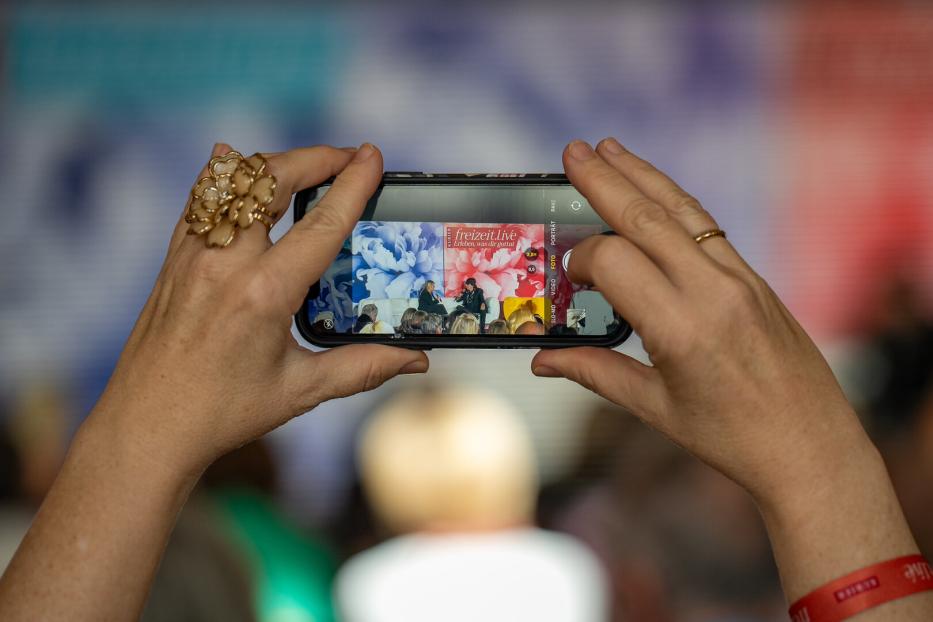 Eine Person fotografiert mit einem Smartphone eine Veranstaltung von „freizeit.live“.