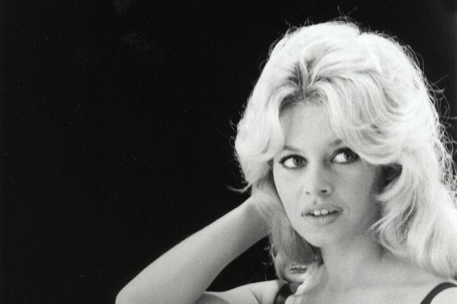 Schwarzweißporträt von Brigitte Bardot in einem schwarzen Kleid vor einem dunklen Hintergrund.