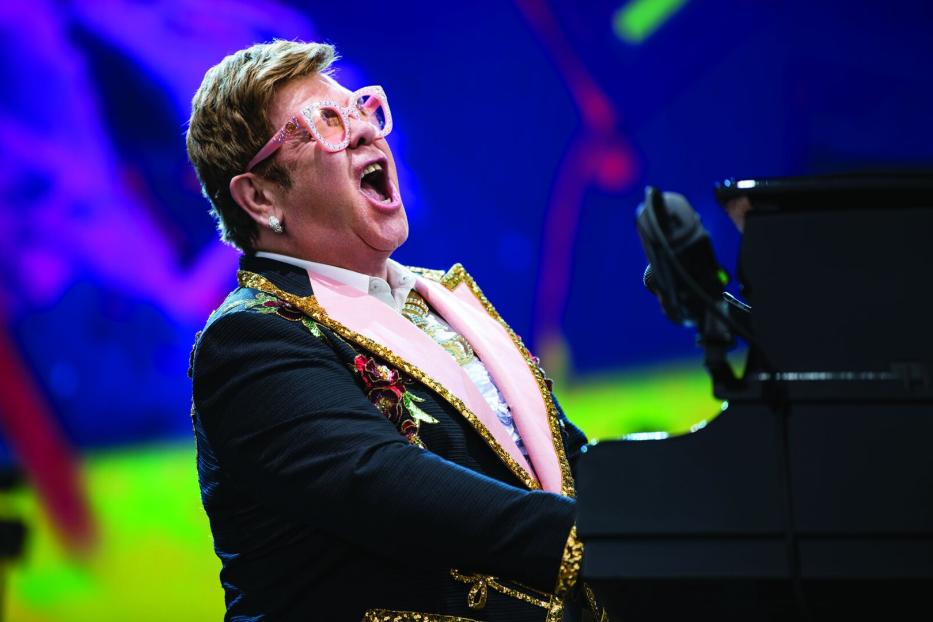 Elton John spielt Klavier und singt mit offenem Mund auf der Bühne.