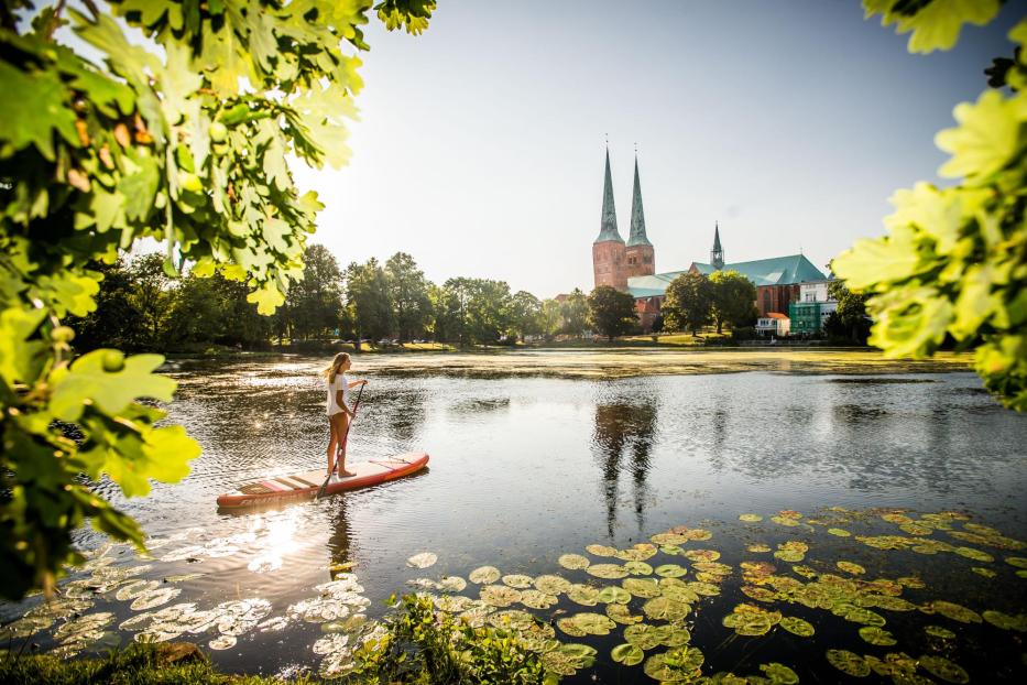 Eine Frau paddelt auf einem See in Lübeck, im Hintergrund die Türme des Doms.