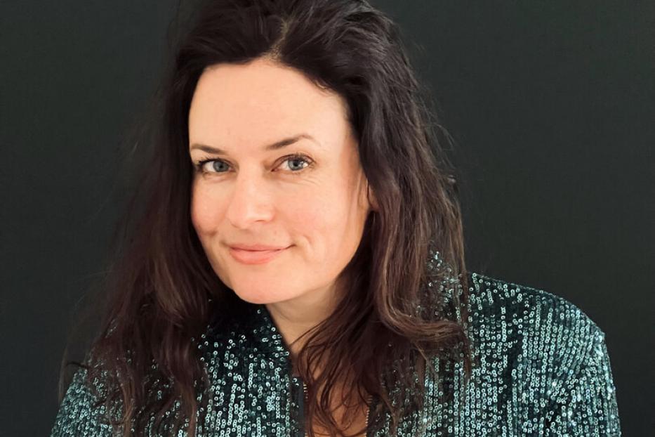Eine Frau mit dunklen Haaren trägt eine glitzernde, grüne Jacke.