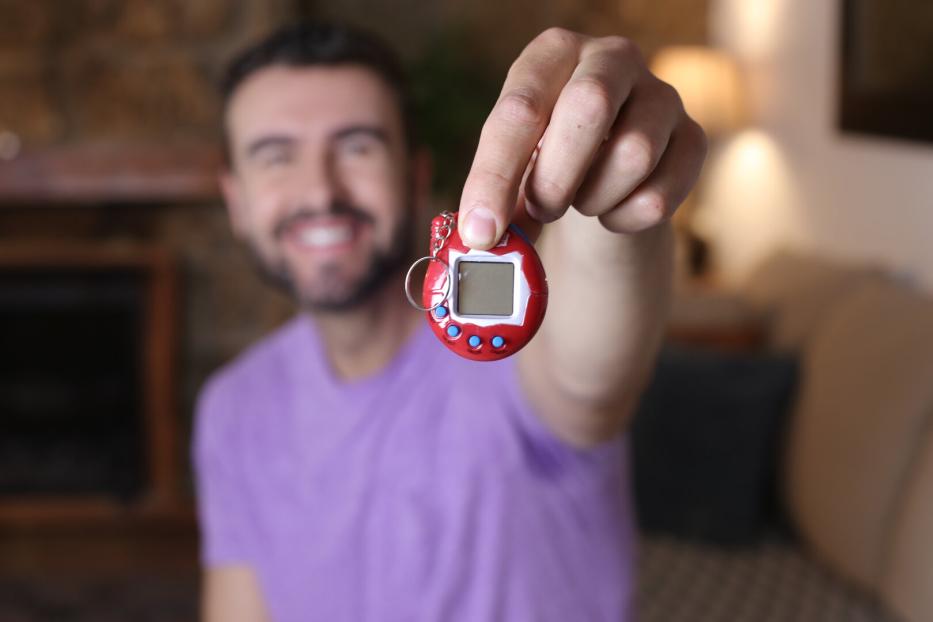 Ein Mann hält ein rotes Tamagotchi in die Kamera.