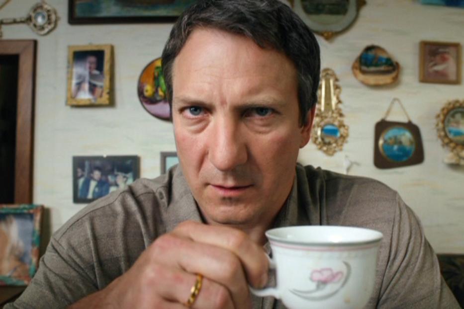 Ein Mann hält eine Teetasse in der Hand und blickt ernst in die Kamera.