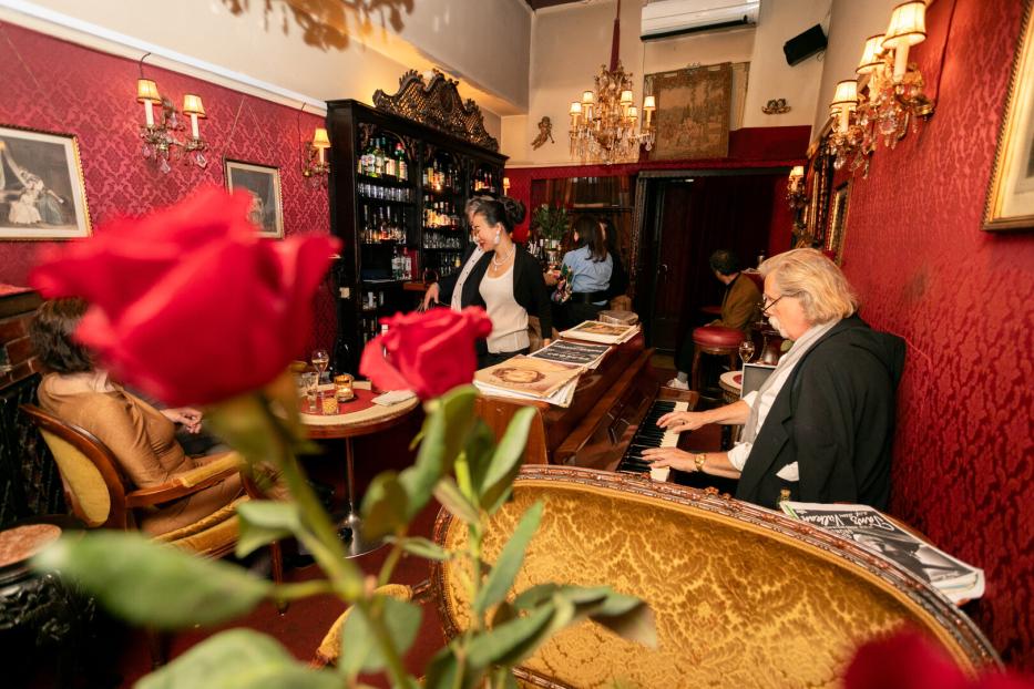 In einer Bar spielt ein Pianist, während eine Barkeeperin Getränke zubereitet.