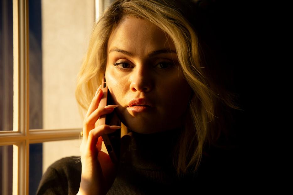 Eine blonde Frau telefoniert am Fenster.