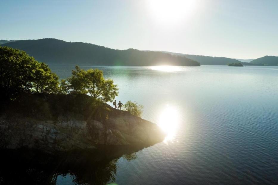 Zwei Personen stehen auf einem Felsen am Ufer eines Sees im Morgenlicht.