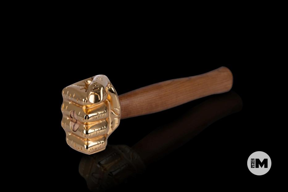 Ein goldener Hammer mit einem Griff aus Holz liegt auf einer schwarzen Oberfläche.