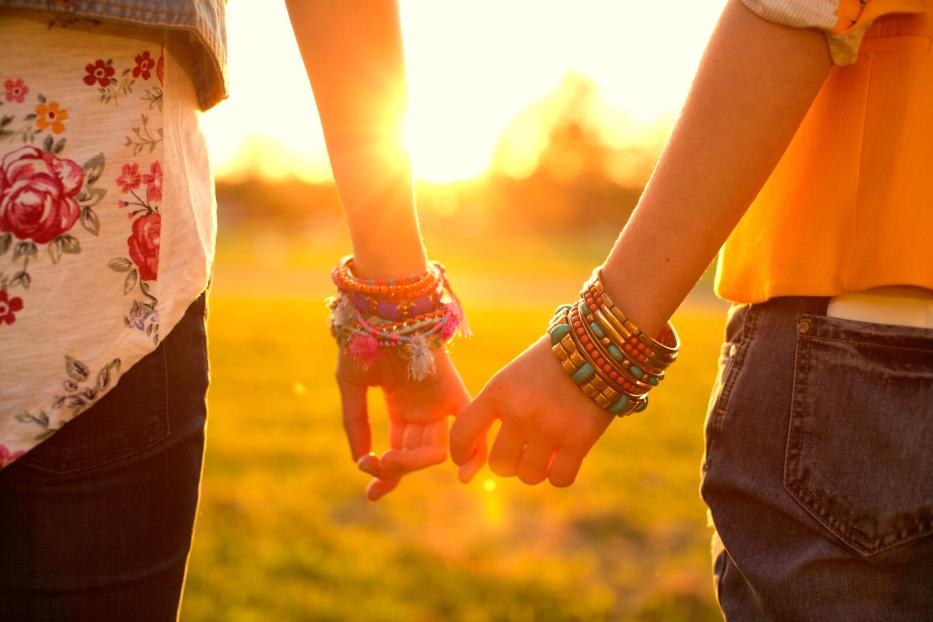 Zwei Personen halten Händchen, beide tragen bunte Armbänder.