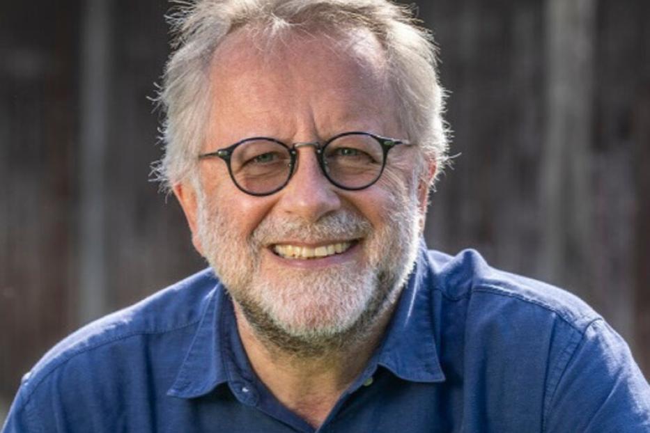 Ein lächelnder Mann mit Brille und Bart trägt ein blaues Hemd.