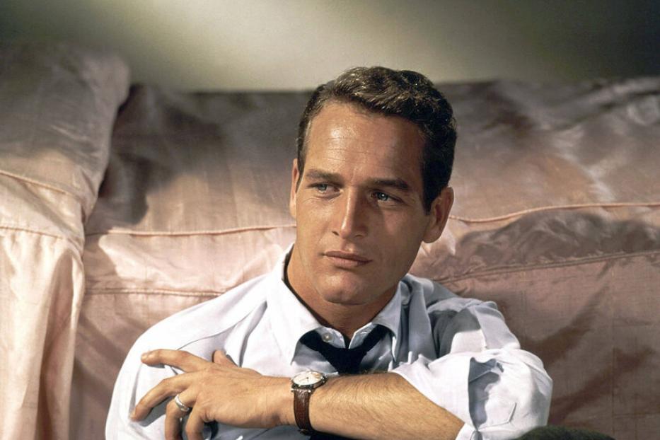 Der Schauspieler Paul Newman sitzt vor einem Bett.