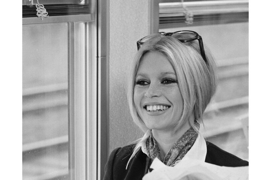 Brigitte Bardot lächelt in einem Zugabteil, mit einer Flasche Champagner im Vordergrund.