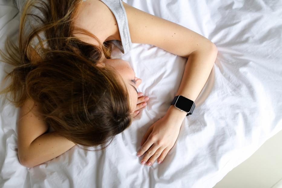 eine Frau liegt schlafend mit einer Smartwatch am Handgelenk im Bett.