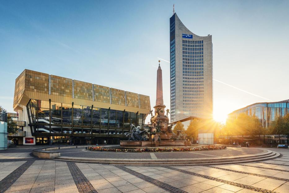 Ein Platz mit einem modernen Hochhaus, einem Brunnen und einem goldenen, verspiegelten Haus.