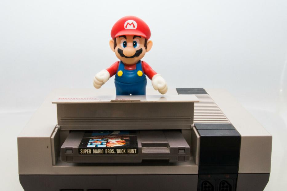Eine Mario-Figur steht auf einer Nintendo-Konsole mit dem Spiel „Super Mario Bros./Duck Hunt“.