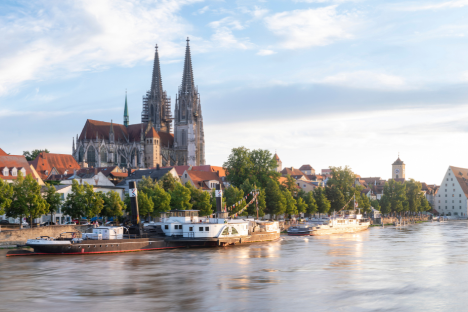 Blick auf die Stadt Regensburg, Deutschland, mit Schiffen, die auf der Donau fahren, umgeben von historischen Gebäuden.