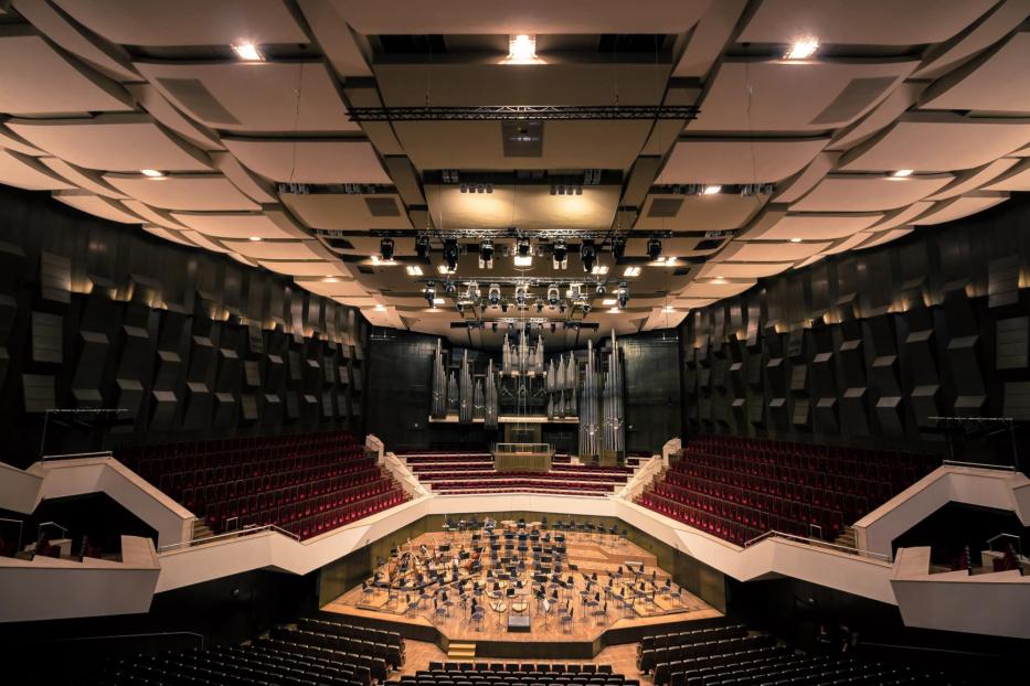 Blick in einen Konzertsaal mit Bühne, Orgel und rotem Gestühl.