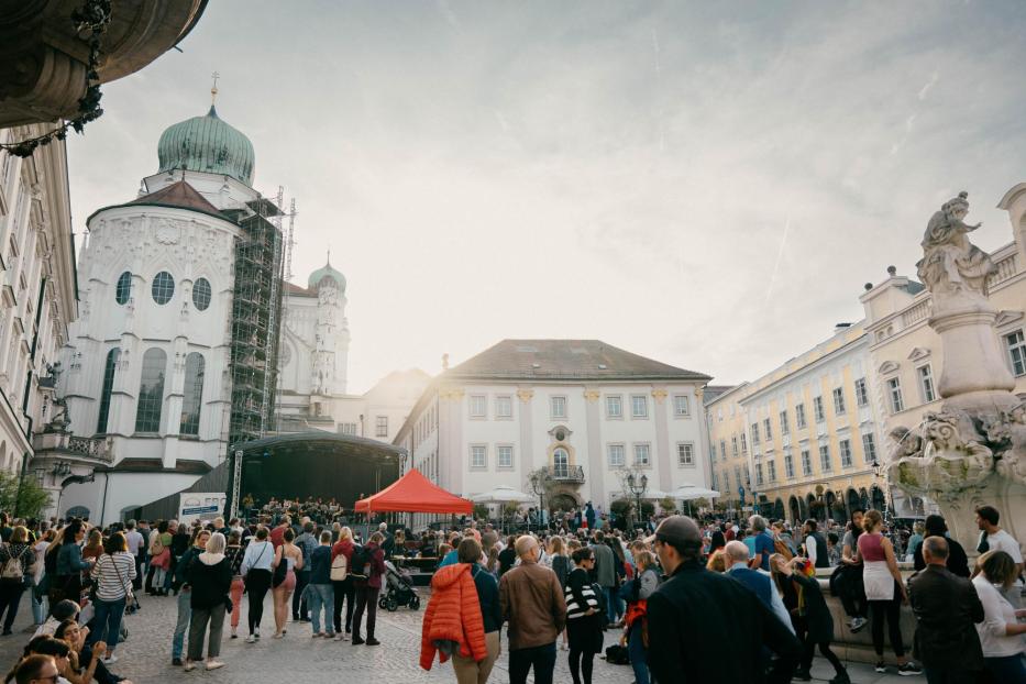 Eine Menschenmenge versammelt sich auf einem Platz vor einer Kirche und einem Brunnen.