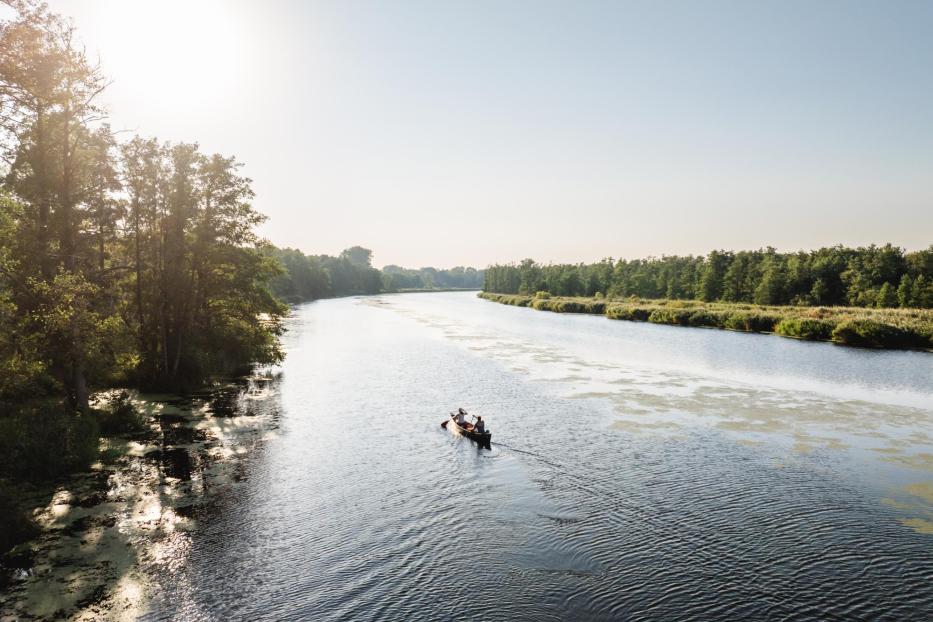 Ein Kanu auf einem breiten Fluss inmitten der Natur im Sonnenuntergang.