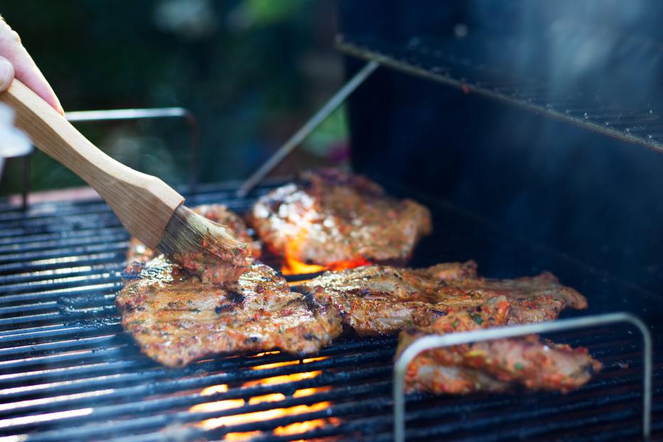 Mit einem Pinsel wird Fleisch auf einem Grill mariniert.