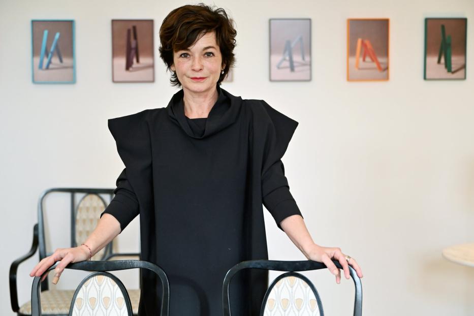 Eine Frau in einem schwarzen Kleid posiert vor einer Wand mit abstrakten Bildern.