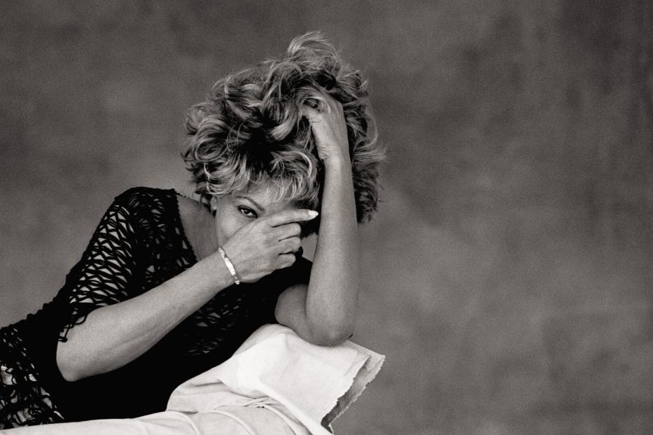Tina Turner, fotografiert von Peter Lindbergh, blickt mit einer Hand vor dem Gesicht in die Kamera.