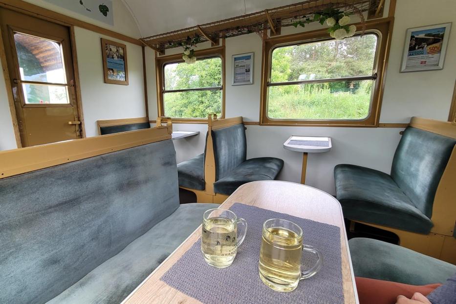 Ein Speisewagen in einem Zug; vorne im Bild ist ein Tisch mit zwei Gläsern Weißwein zu sehen.