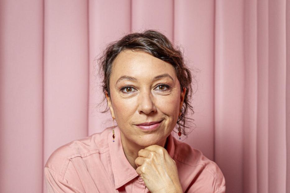 Ursula Strauss sitzt vor einem rosa Hintergrund.