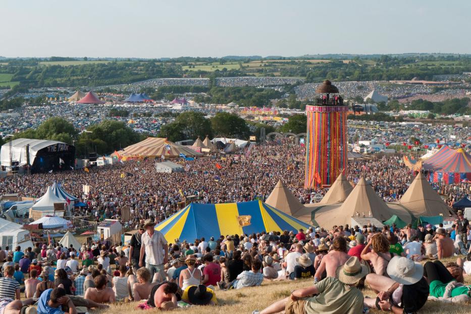 Blick über das Glastonbury Festival mit Menschenmassen, Bühnen und Zelten.