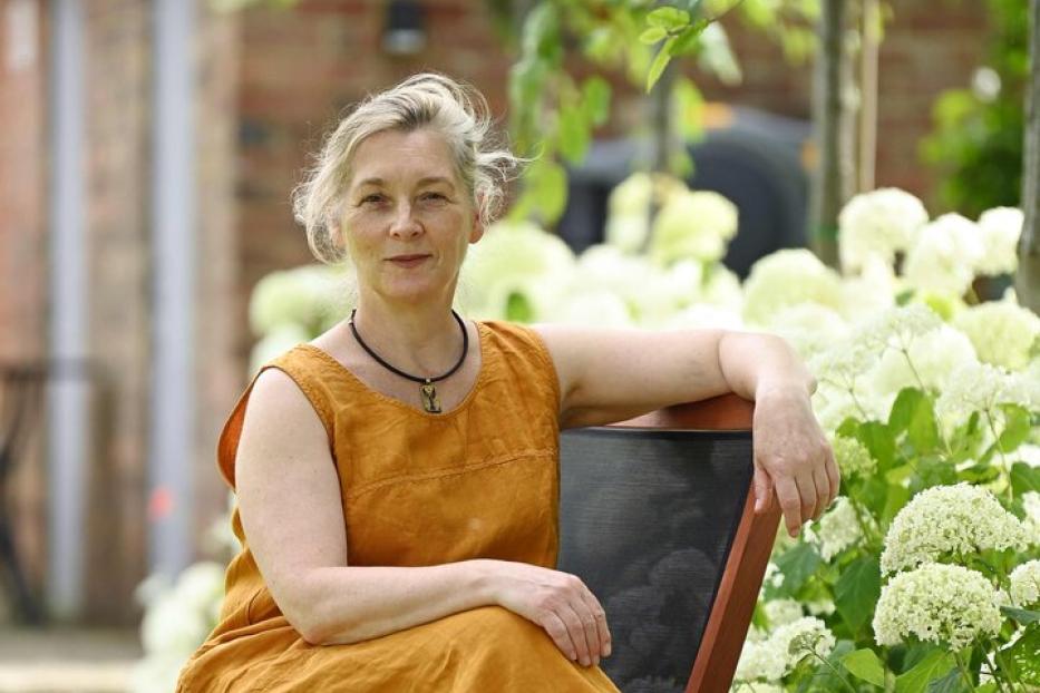 Eine Frau sitzt auf einem Stuhl neben weißen Hortensien in einem Garten.