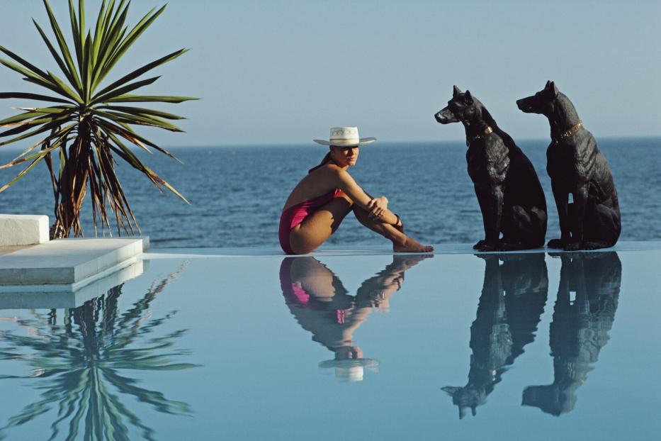 Eine Frau sitzt am Pool, hinter ihr liegt das weite Meer.