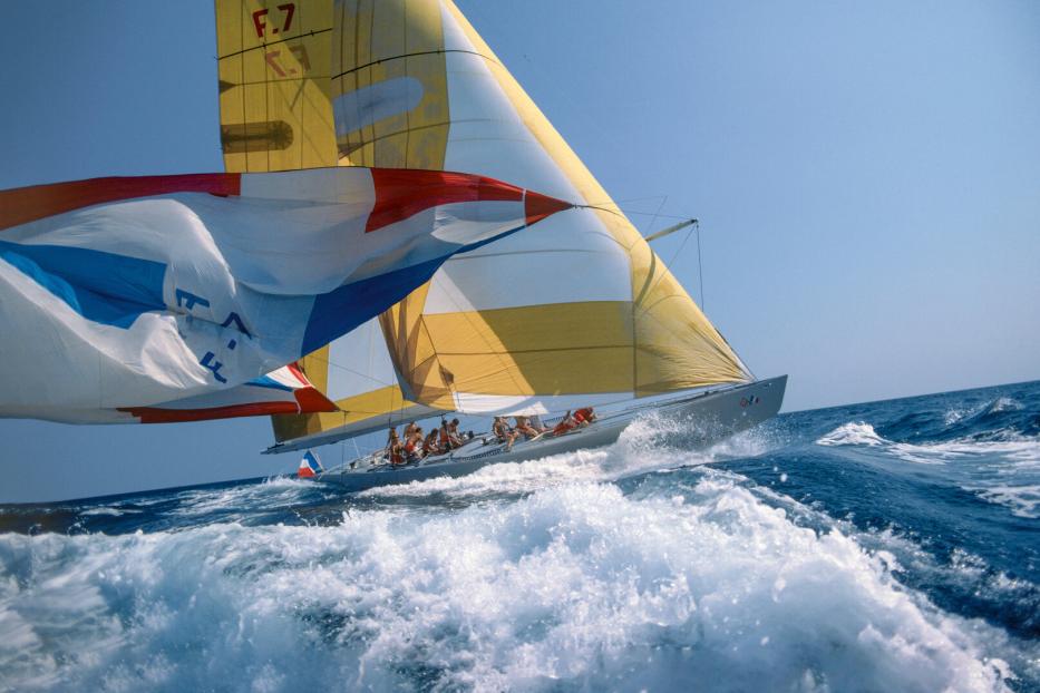 Ein Segelboot mit gelb-weißen Segeln fährt durch aufgewühltes, blaues Wasser.
