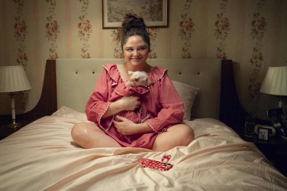 Eine Frau sitzt auf einem Bett und hält ein kleines, weißes Tier im Arm.