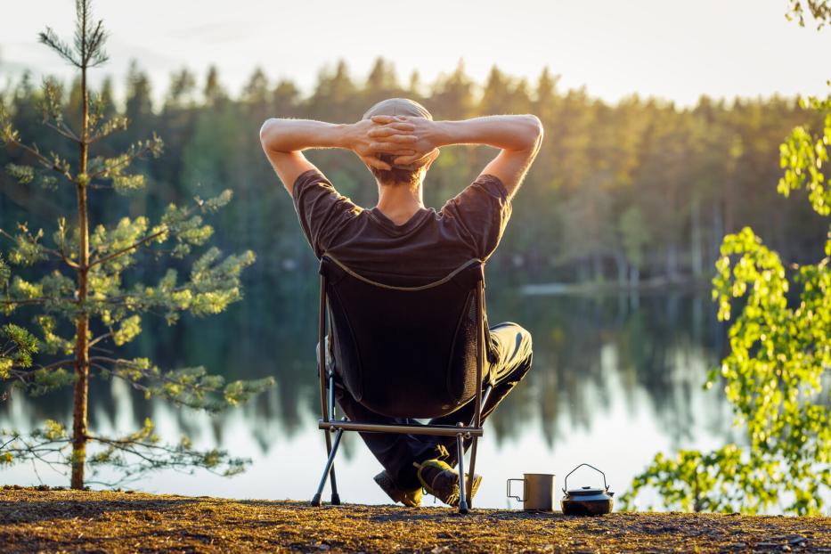 Ein Mann sitzt an einem See in einem Campingstuhl an einem schönen Sommerabend.