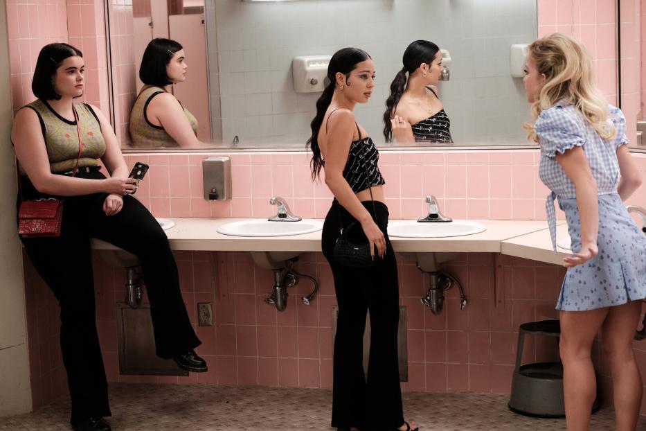 Drei junge Frauen stehen in einem Badezimmer mit rosa Fliesen vor einem Spiegel.