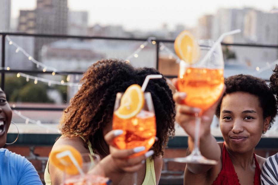 Freunde - offenbar in einer Rooftop-Bar - prosten einander mit Aperol Spritz zu.
